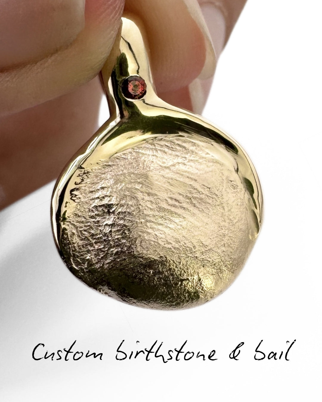 Close up of gold fingerprint pendant with garnet gemstone set in the bail