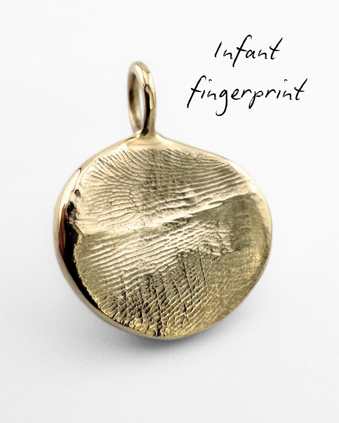 Close up of gold pendant with a babies fingerprint impression on a light grey background