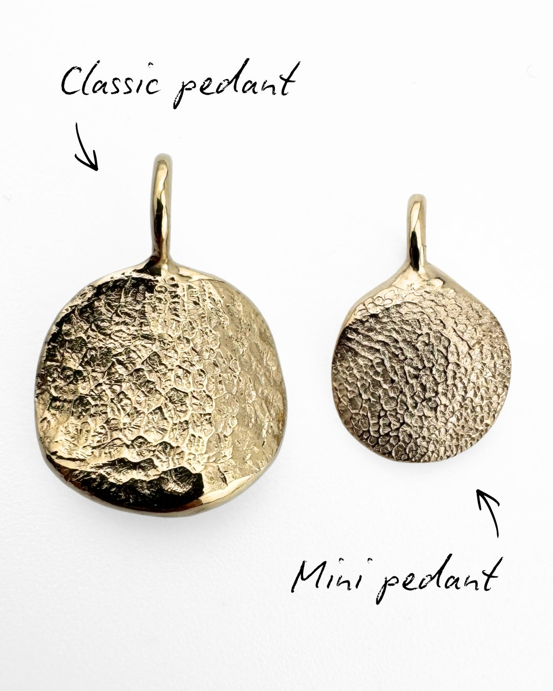 Close up of two gold pendants with dog's nose print and paw print impressions on light grey background