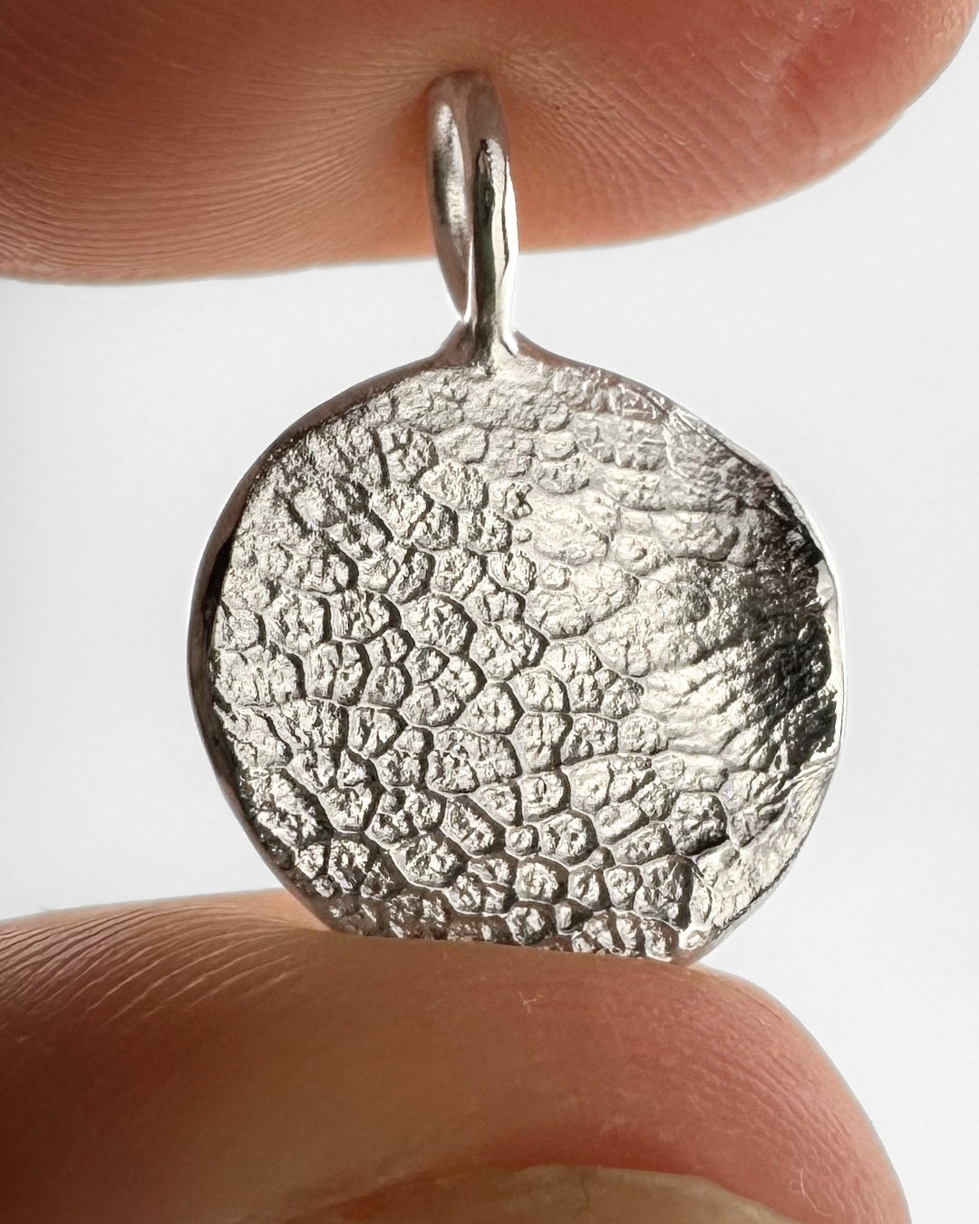 Close up of silver pendant with dog's nose print impression on light grey background