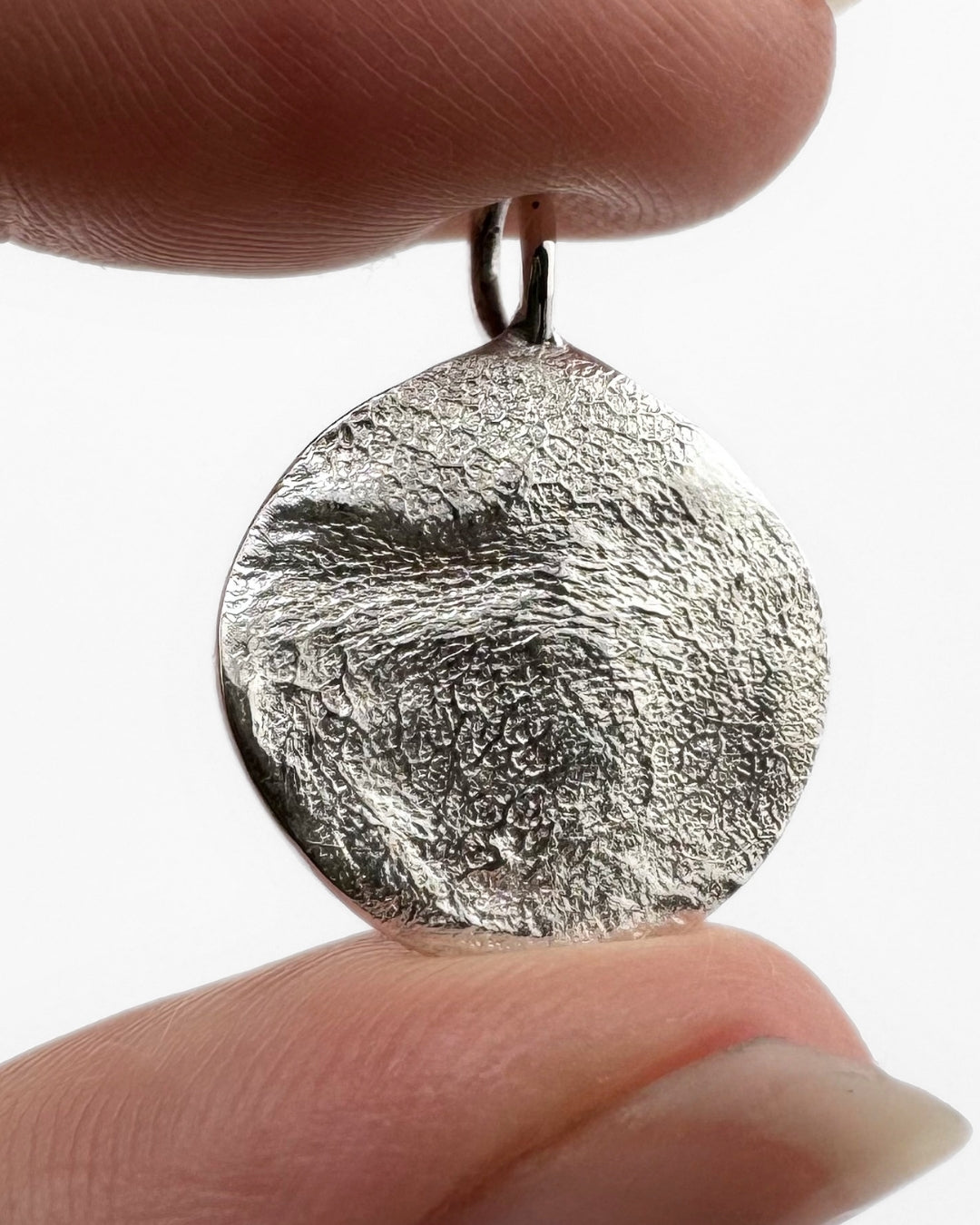 Close up of silver pendant with dog's nose print impression on light grey background