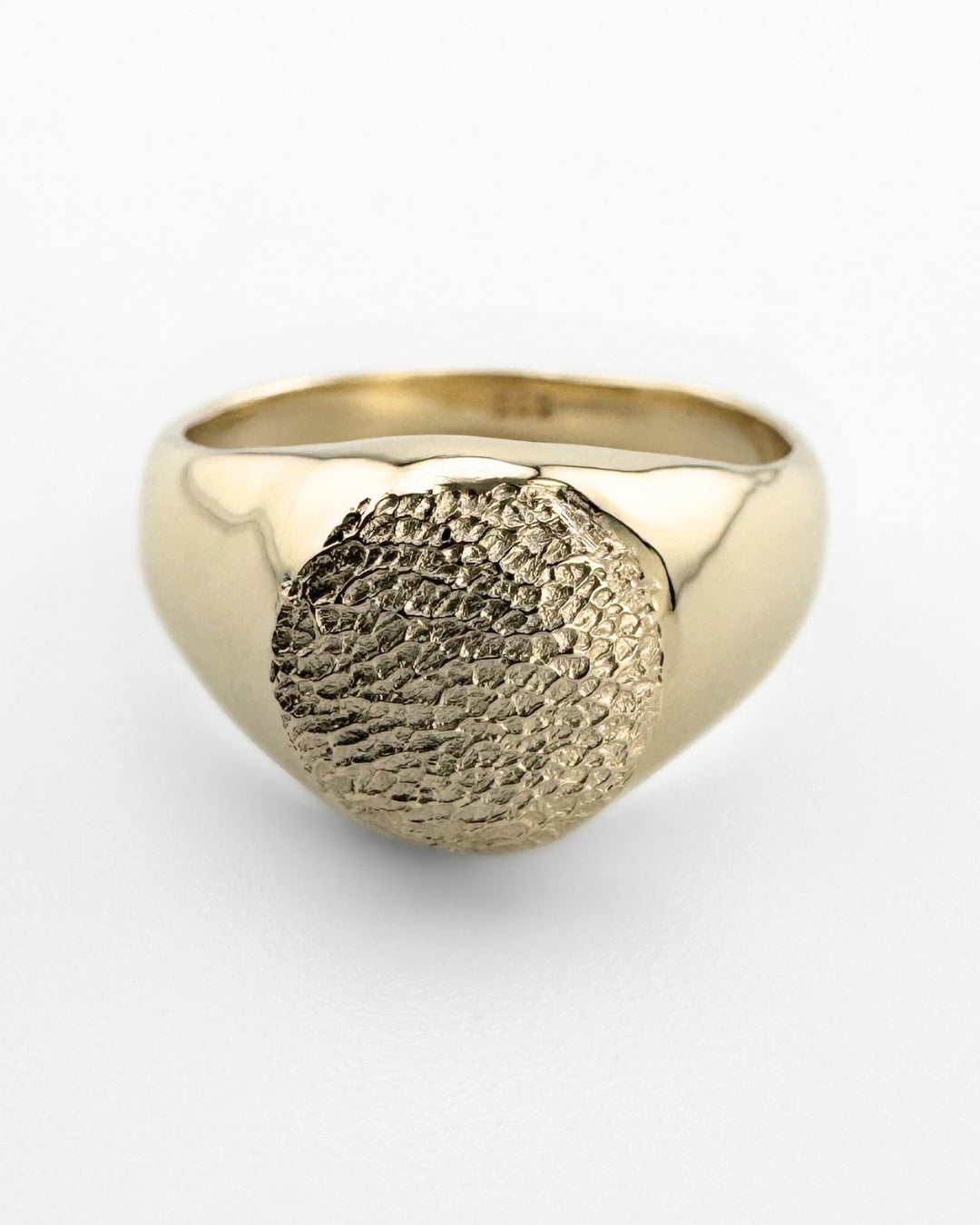 Close up of gold signet ring with dog's paw print impression on light grey background
