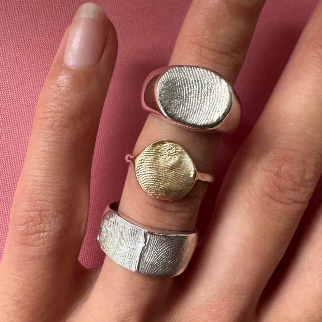A person wearing two sterling silver and one 9ct gold fingerprint impression rings