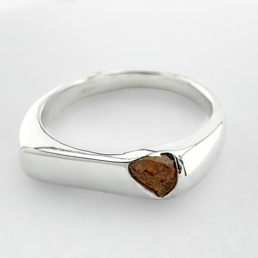 Thin silver signet ring with a honey coloured sapphire on a light grey background