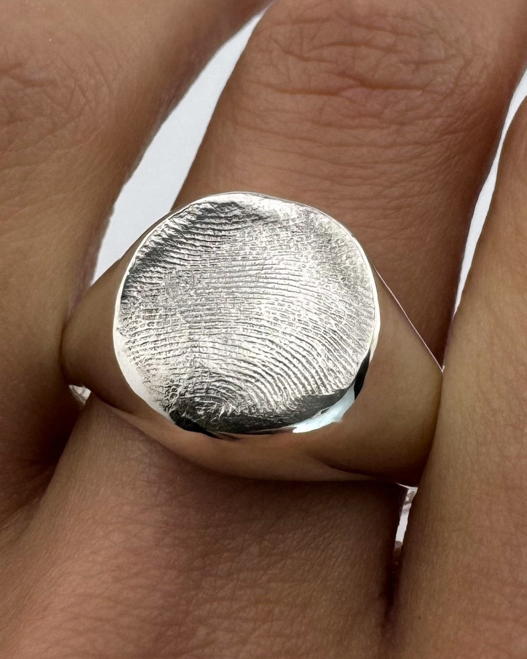 Close-up of hand wearing a large silver signet ring with fingerprint impression