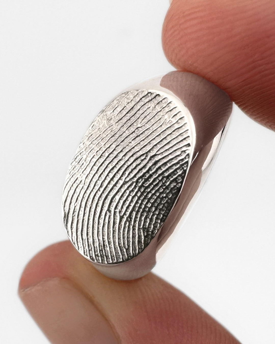 Close-up of a silver oval signet ring with fingerprint impression