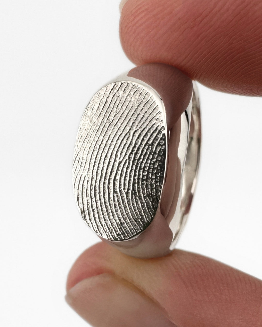 Close-up of a silver oval signet ring with fingerprint impression