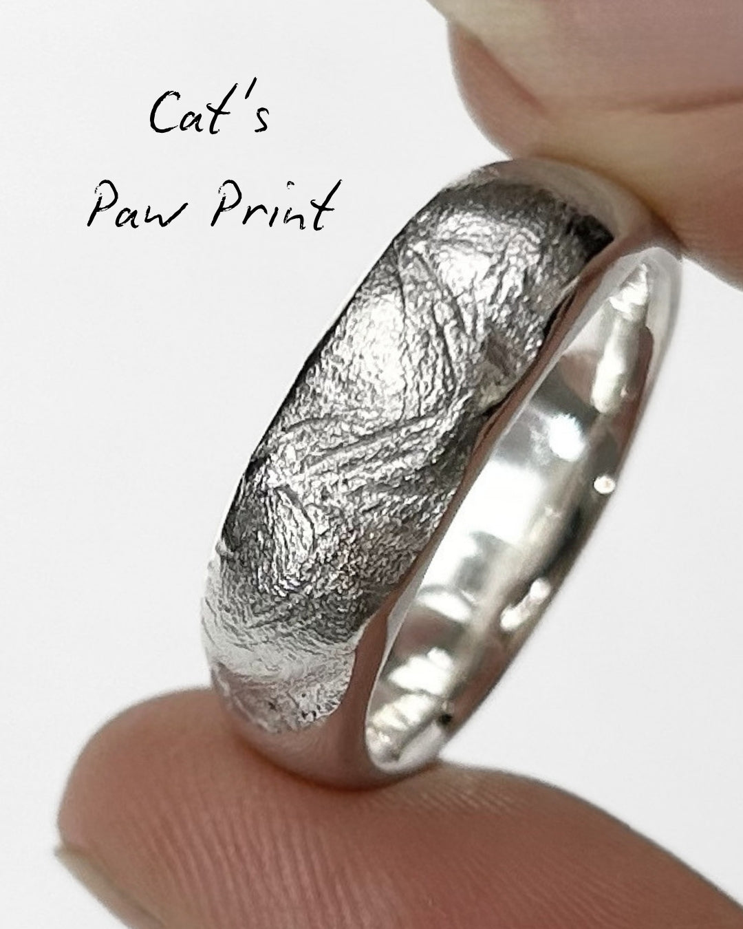 Close-up of silver ring band with a cat's paw print impression on light grey background