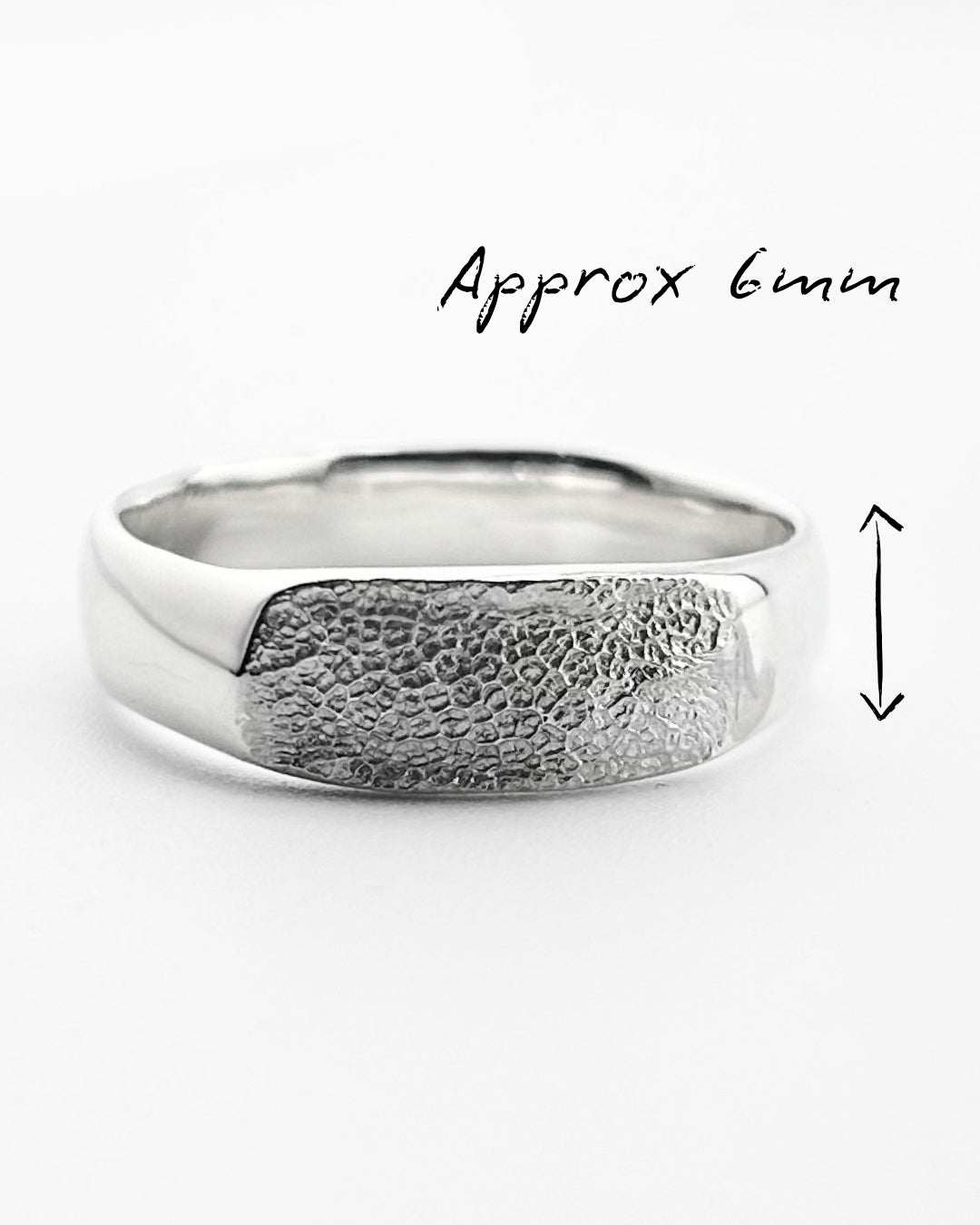 Close-up of silver ring band with a dog's nose print impression on light grey background