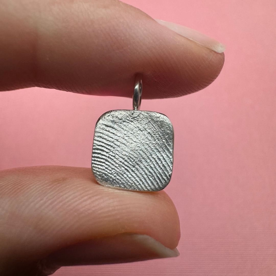 Person holding a square silver fingerprint impression pendant