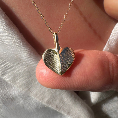 Thumb holding gold heart fingerprint necklace