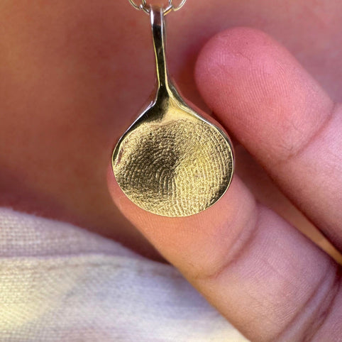 Hand holding gold fingerprint necklace