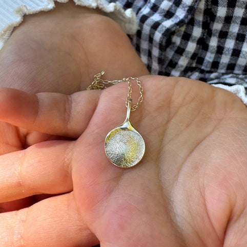 Child holding a gold fingerprint pendant