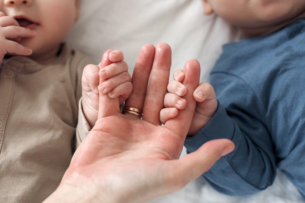 Close up of two babies holding onto mums hands