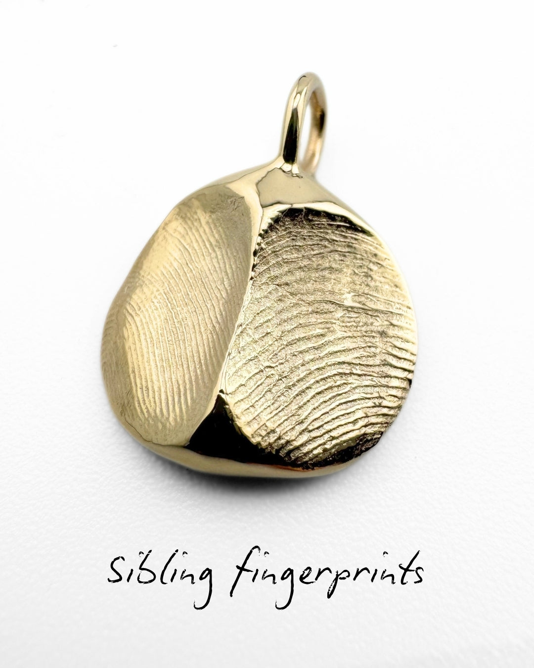 Close up of gold pendant with two fingerprint impressions side-by-side on a light grey background