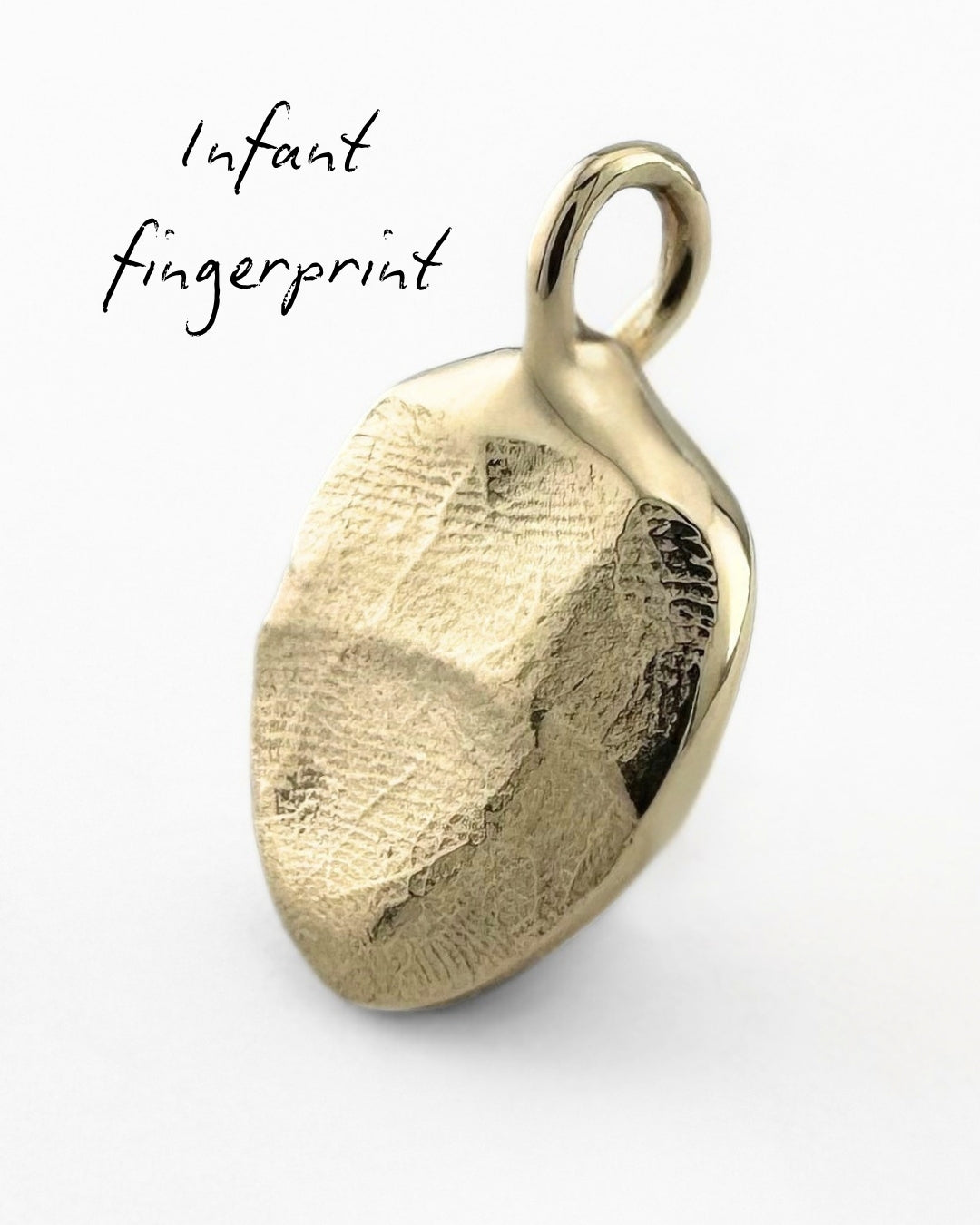 Close up of gold pendant with a babies fingerprint impression on a light grey background