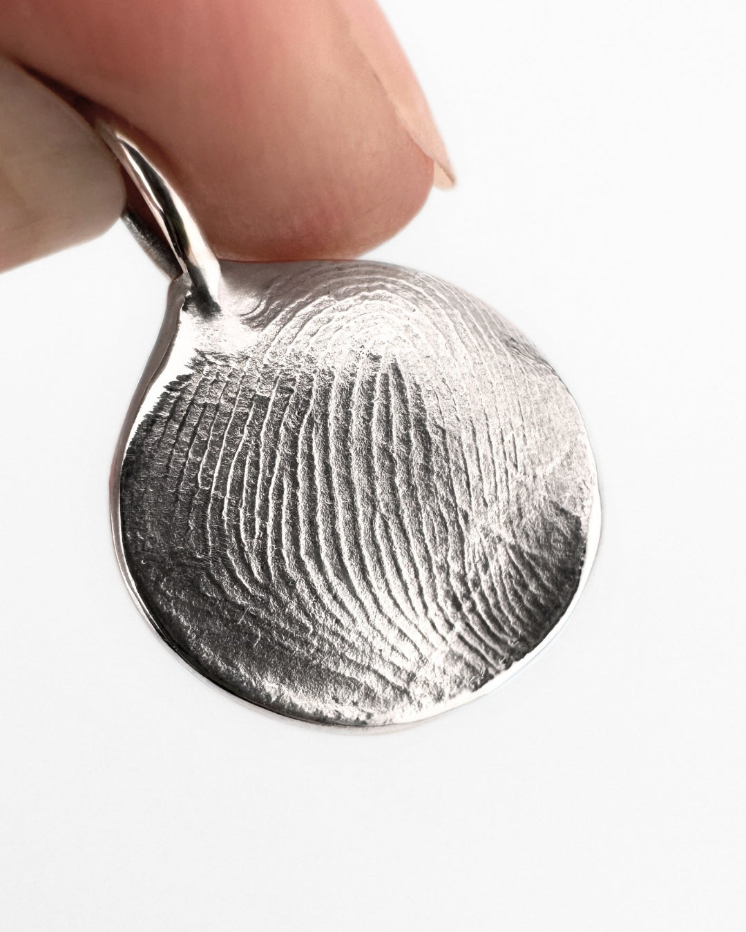 Close up of a silver fingerprint pendant on a light grey background