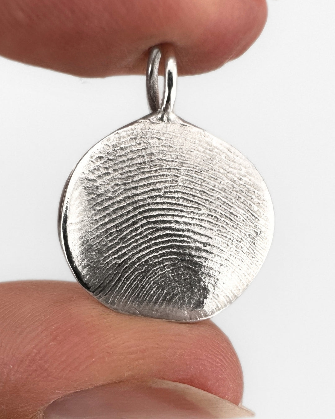 Close up of a silver fingerprint pendant on a light grey background