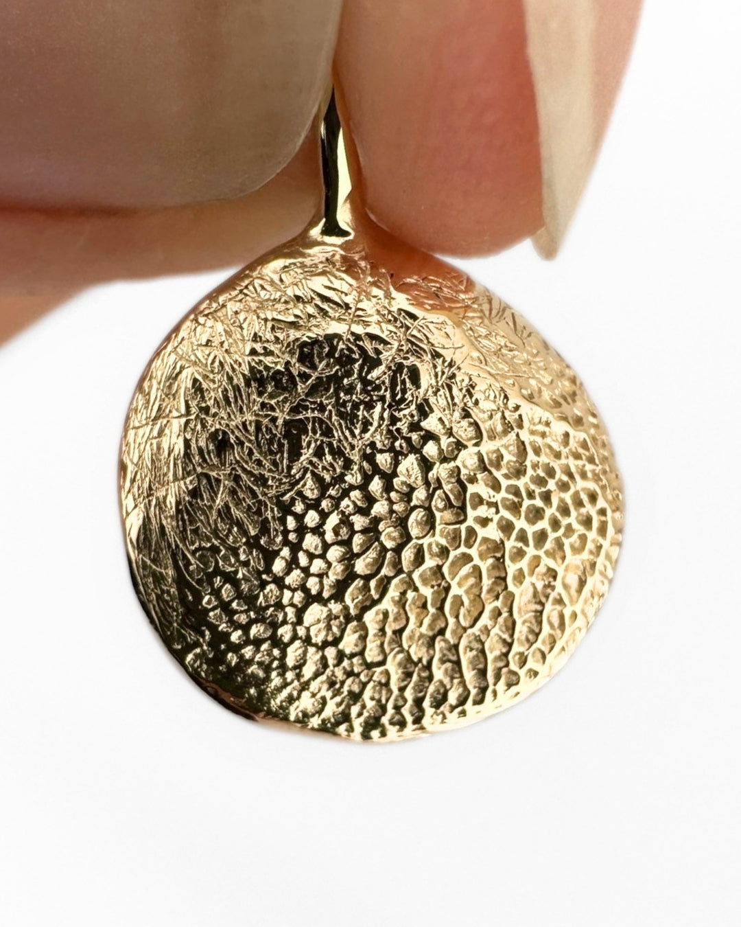 Close up of gold pendant with dog's paw print impression on light grey background