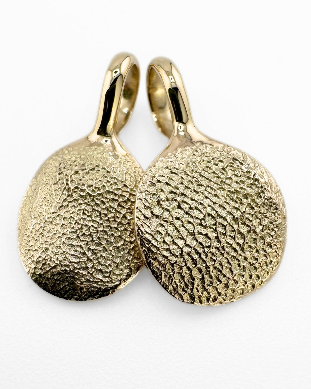 Close up of two gold pendants with dog's paw print impressions on light grey background