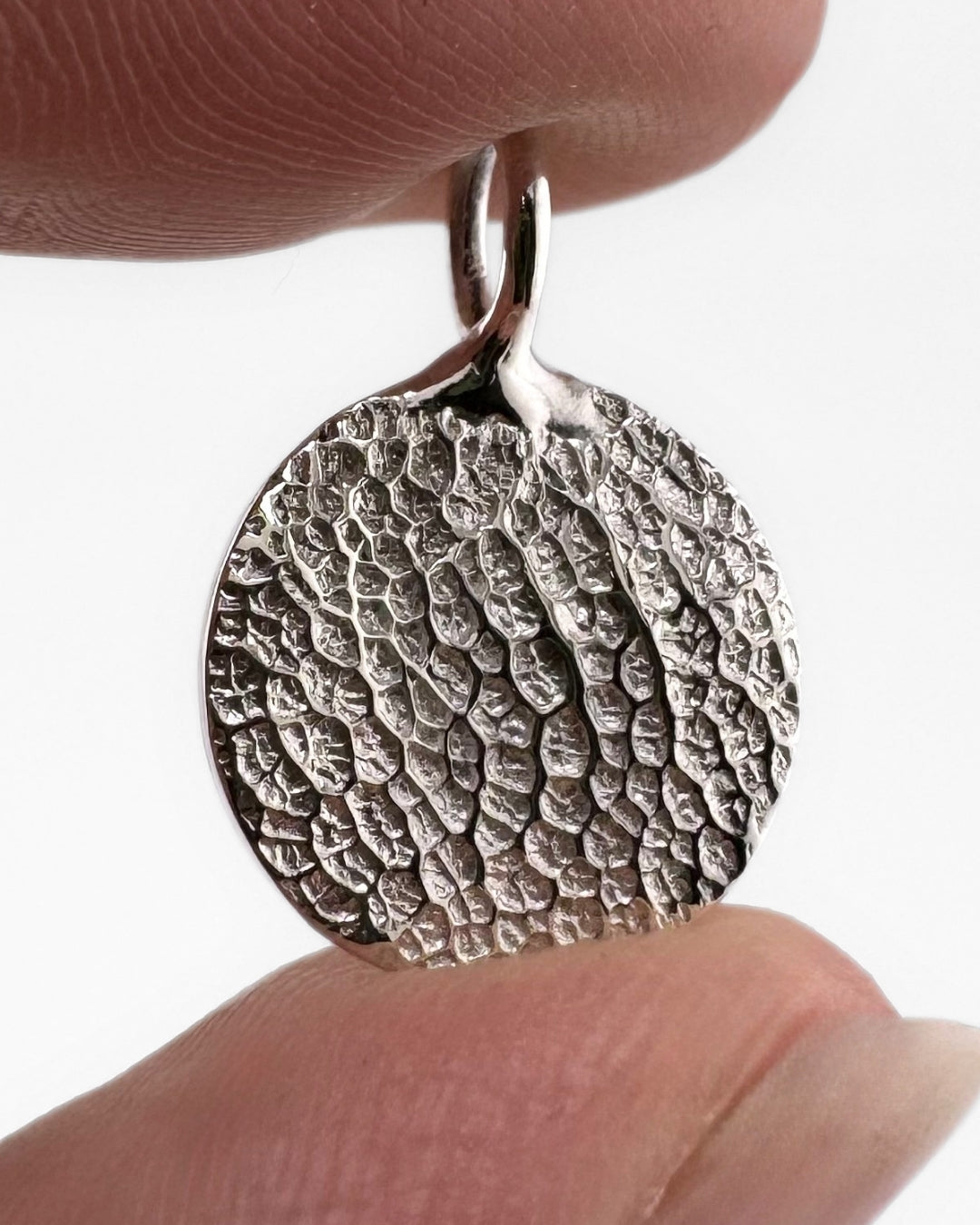 Close up of silver pendant with dog's nose print impression on light grey background