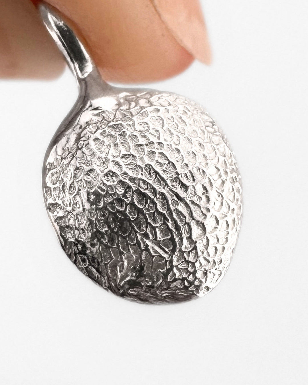 Close up of silver pendant with dog's paw print impression on light grey background