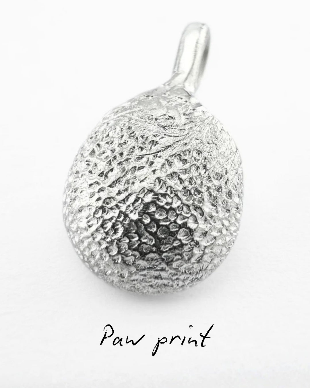 Close up of silver pendant with dog's paw print impression on light grey background