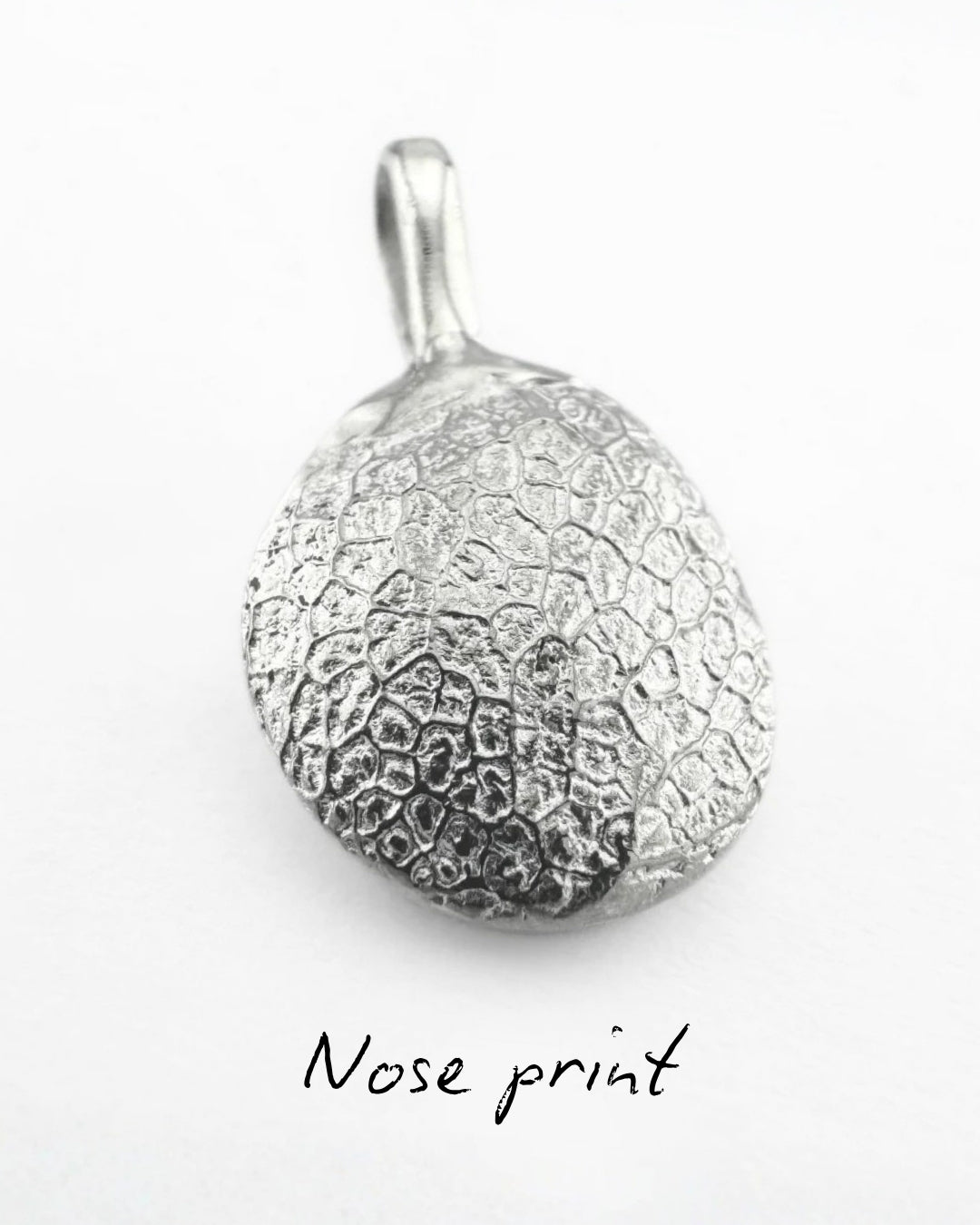 Close up of silver pendant with dog's nose print impression on light grey background