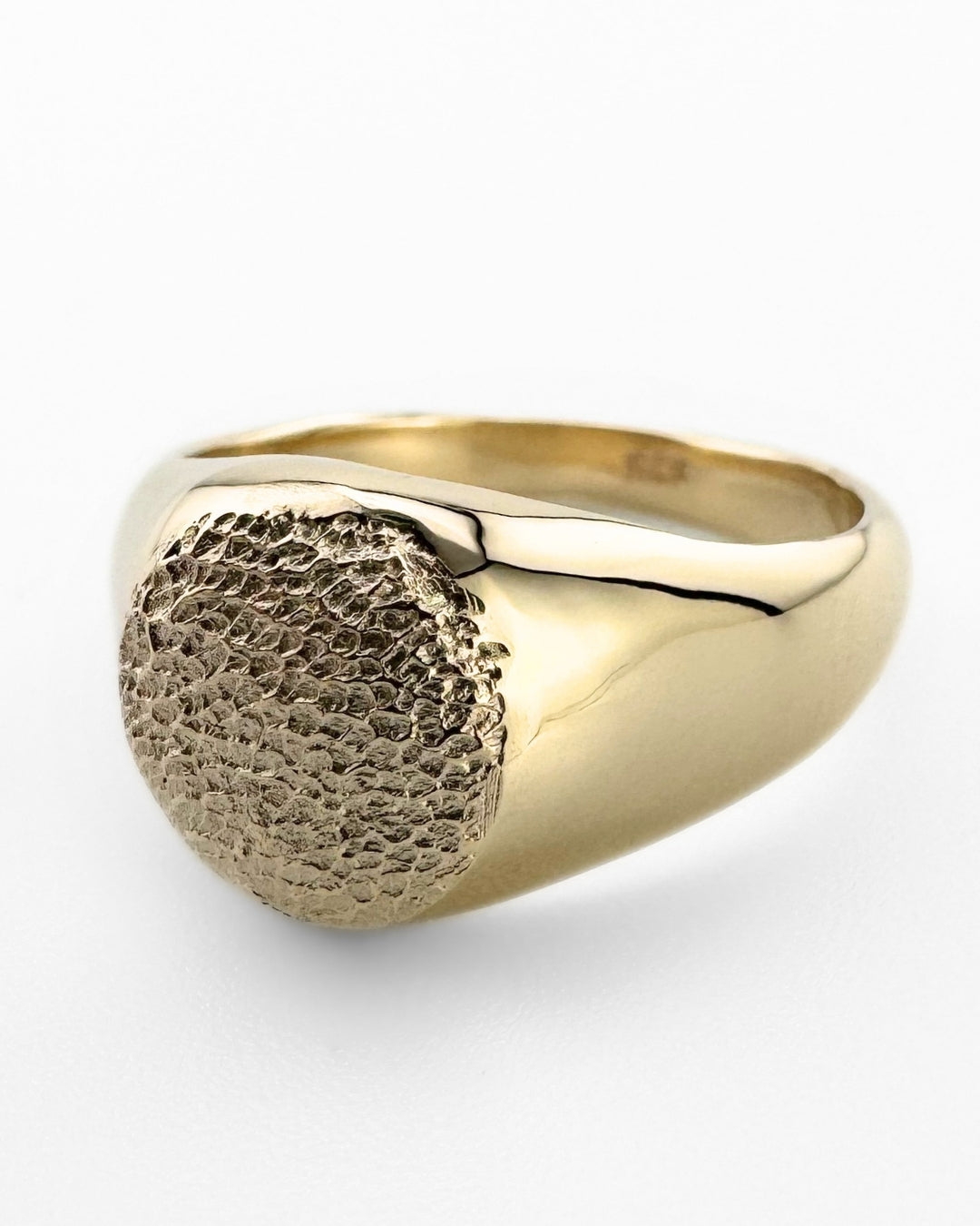 Close up of gold signet ring with dog's paw print impression on light grey background