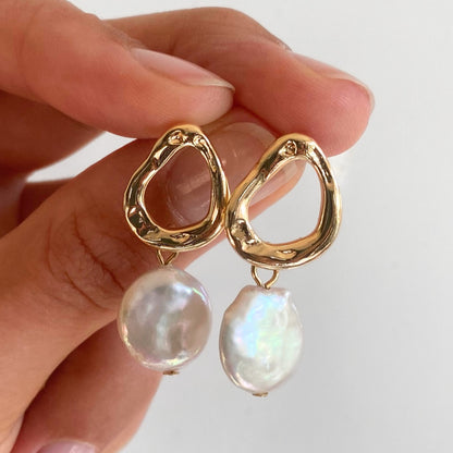 Person holding gold teardrop earrings with flat freshwater pearls