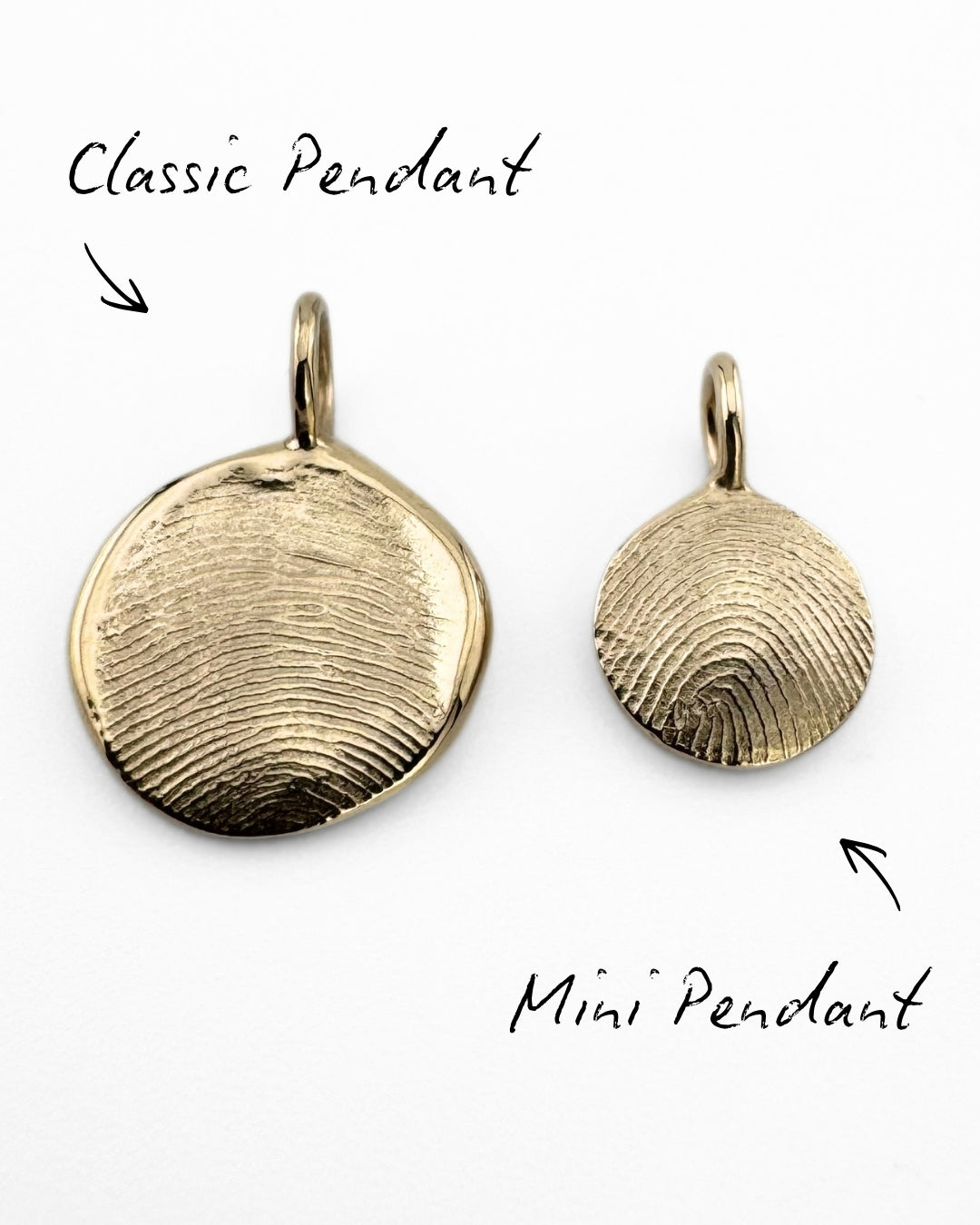 Close up of two gold fingerprint pendants on a light grey background