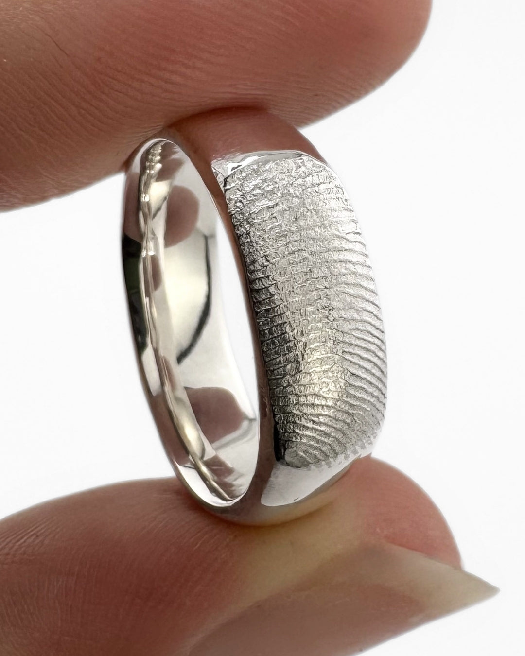 Close up of silver fingerprint ring band on a light grey background
