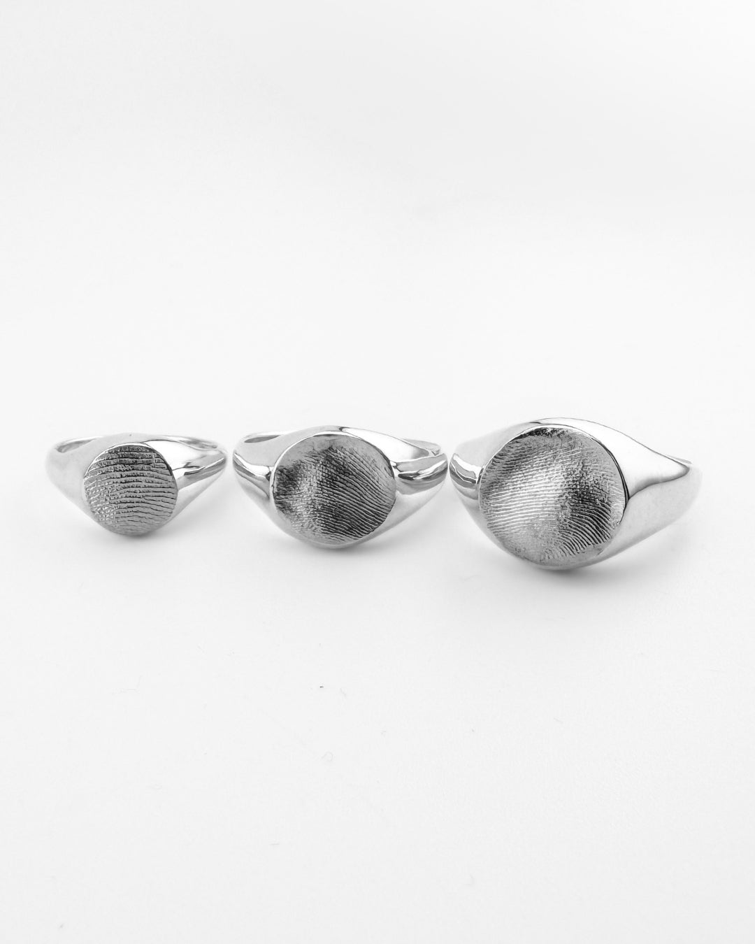 Mini, Classic and Large fingerprint signet rings on a light grey background
