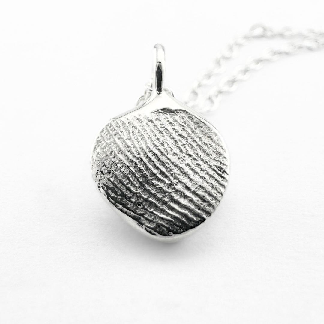Close up of silver fingerprint pendant on light grey background