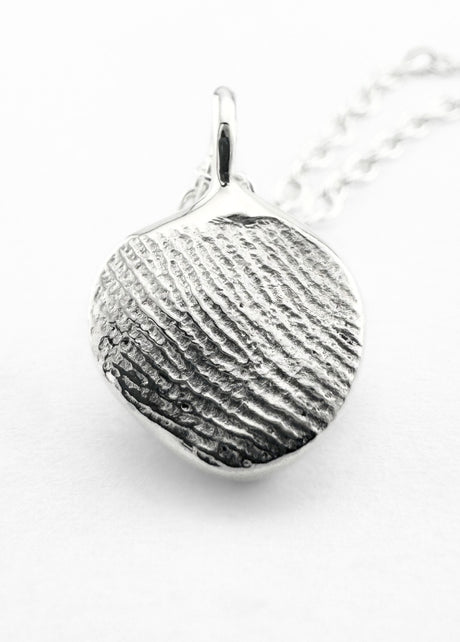 Close up of silver fingerprint pendant on light grey background