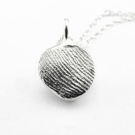 Close up of silver fingerprint pendant on light grey background