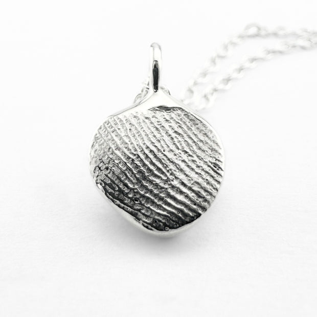 Close up of silver fingerprint pendant on light grey background