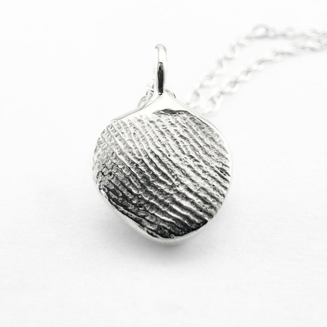 Close up of silver fingerprint pendant on light grey background
