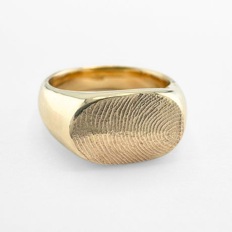 Gold fingerprint signet ring on light grey background