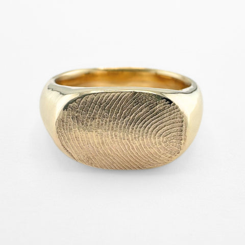 Gold fingerprint signet ring on light grey background