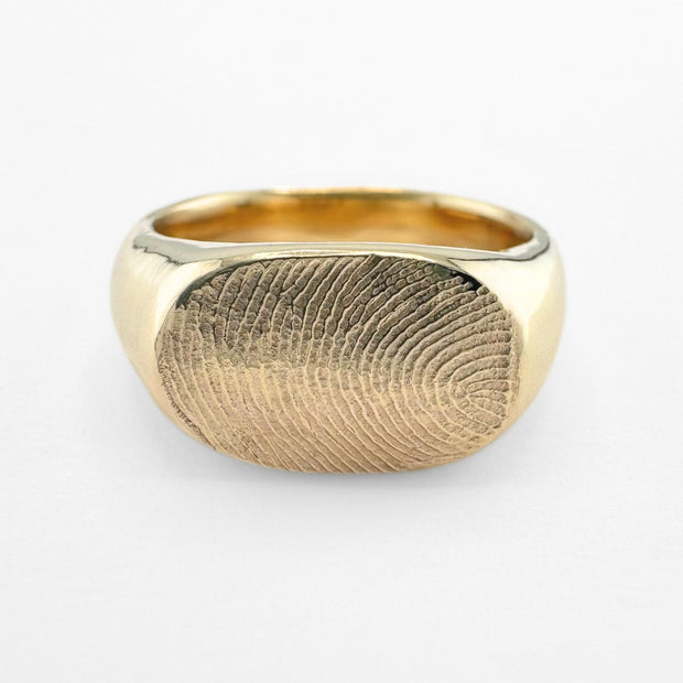 Gold fingerprint signet ring on light grey background