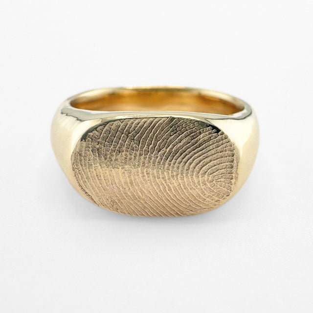 Gold fingerprint signet ring on light grey background