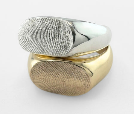 Gold and silver fingerprint signet rings on light grey background