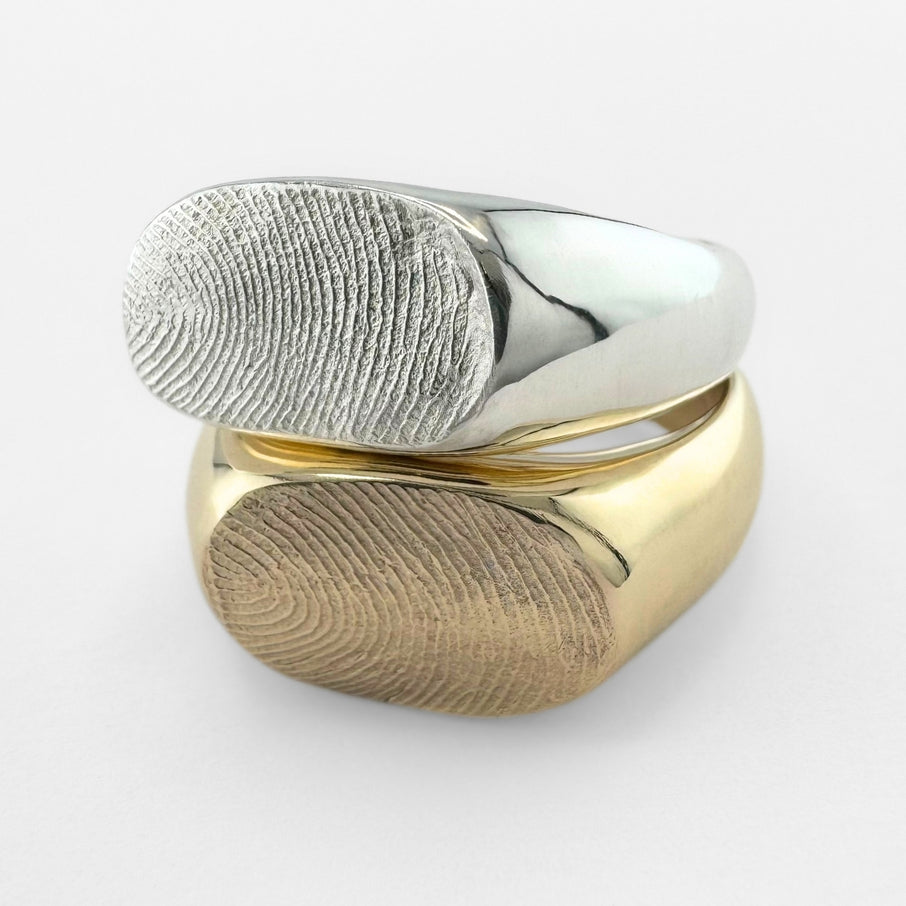 Gold and silver fingerprint signet rings on light grey background