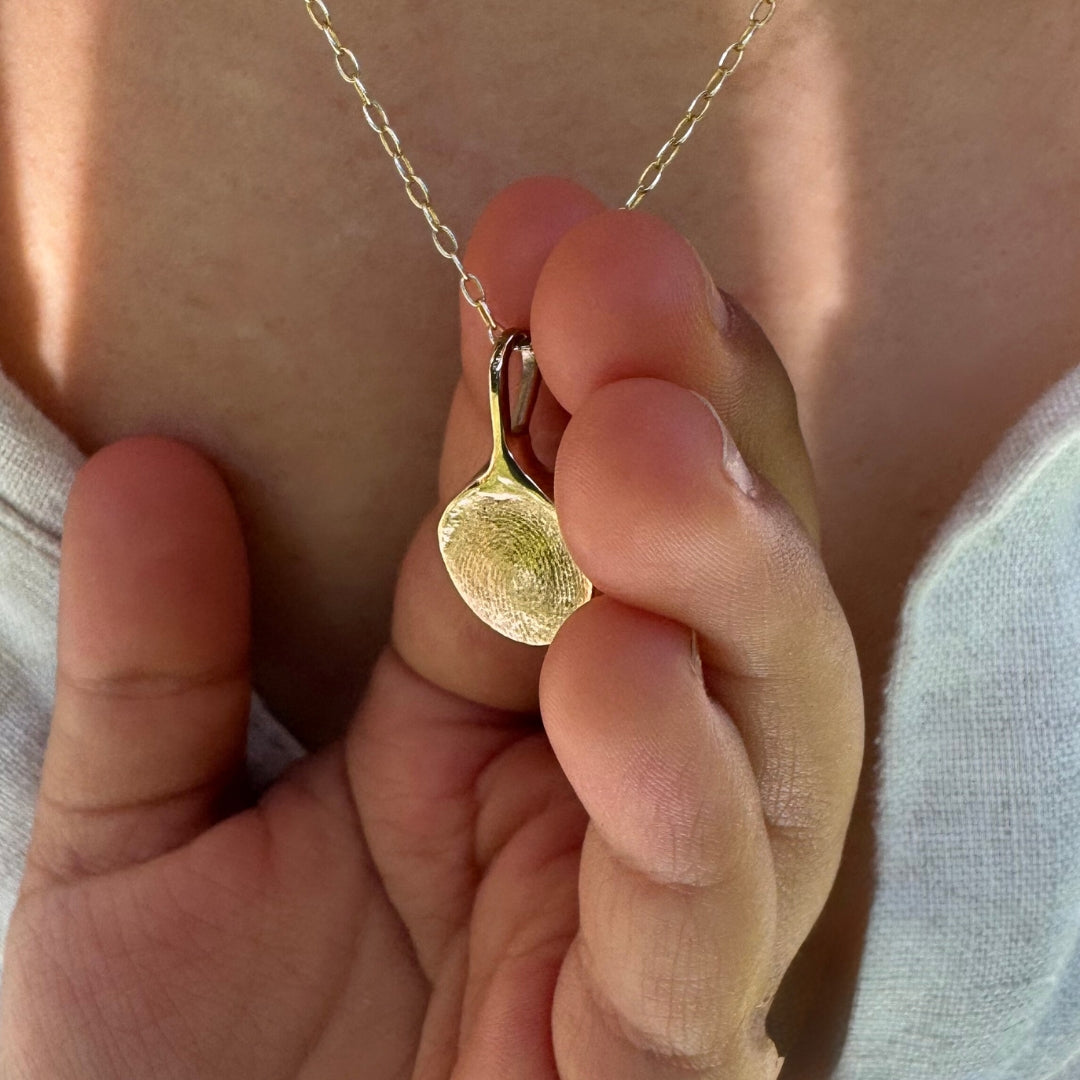 Close up of child holding a gold fingerprint necklace around mums neck
