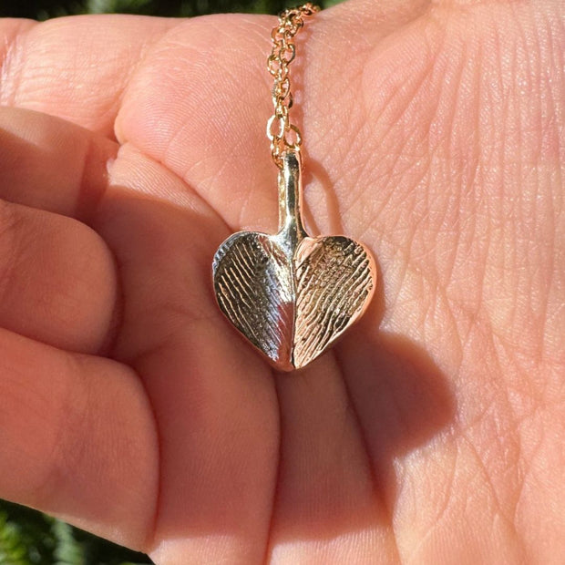 Close-up of a gold heart-shaped fingerprint pendant in the palm of a hand