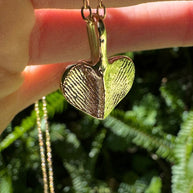 Close up of gold heart shaped fingerprint pendant on green leafy background
