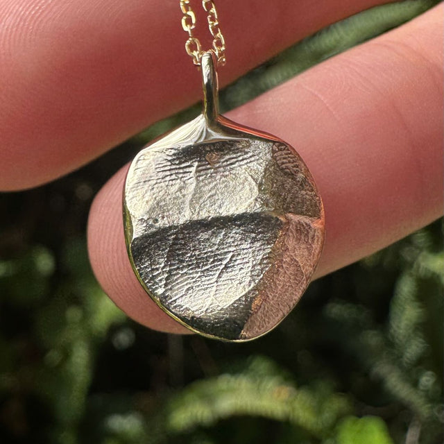 Close up of gold infant fingerprint pendant on green leafy background