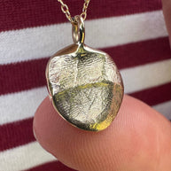 Close up of person wearing gold infant fingerprint pendant on red and white stripped top
