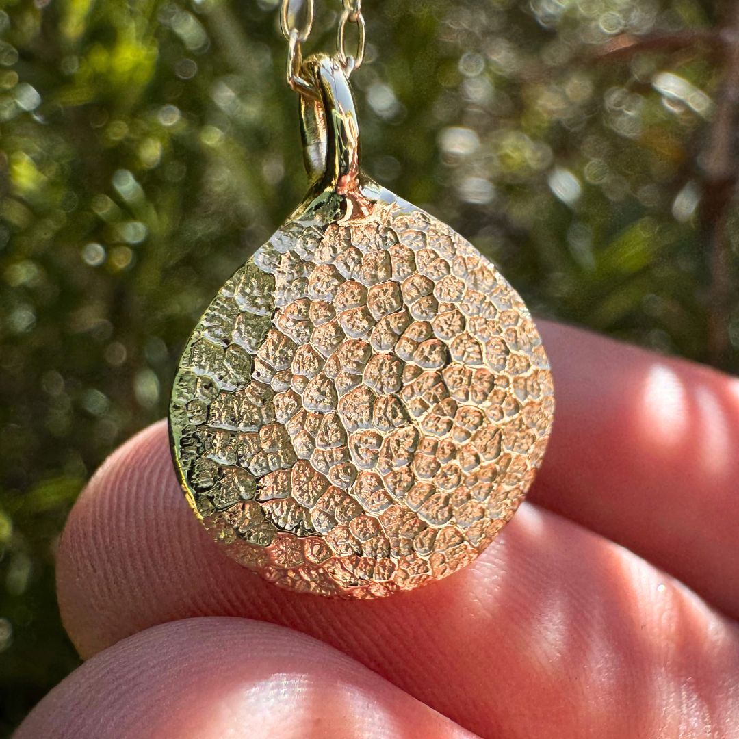 Close up of gold dog's nose print pendant on green leafy background